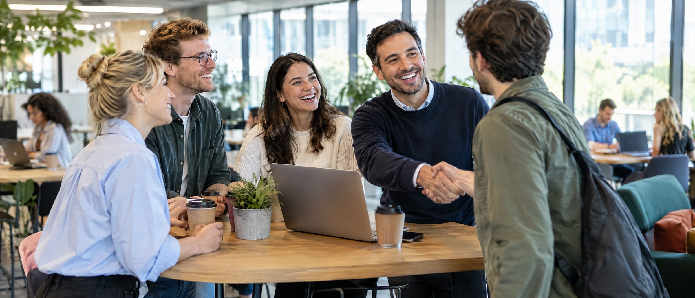 A team welcoming a new colleague with a handshake around a table in a bright office